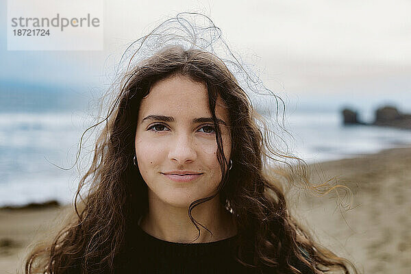 Teenager-Mädchen lächeln  während der Wind ihr Haar am Strand aufhebt