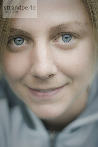 Soft-Nahaufnahme-Porträt einer zufriedenen jungen Frau mit blauen Augen  die eine blaue Fleecejacke trägt.