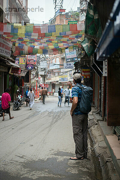 Junger Mann mit Rucksack steht mit Himalaya-Flagge auf der Straße Asiens