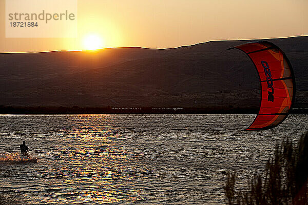 Die Silhouette eines männlichen Kiteboarders mit Sonnenuntergang und Wüstenbergen.