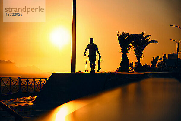 Silhouette eines jungen springenden Skateboardfahrers beim Reiten  Sommersonnenuntergang