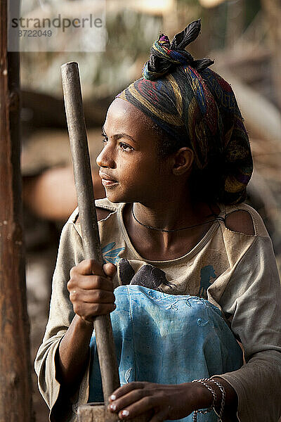 Ein äthiopisches Mädchen zerkleinert Getreide mit einem Stößel zu Hause entlang der Straße zum Simien-Mountains-Nationalpark im Norden Äthiopiens.