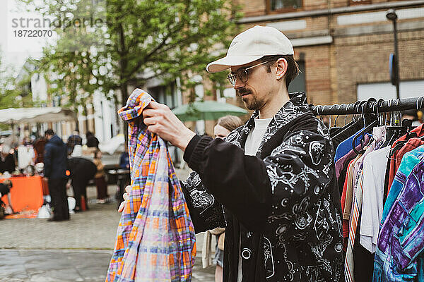 Mann mit Mütze faltet Second-Hand-Kleidung zum Verkauf auf dem Straßenmarkt
