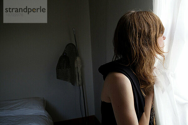 Eine junge Frau schaut aus dem Fenster ihres Schlafzimmers  Los Angeles  Kalifornien.