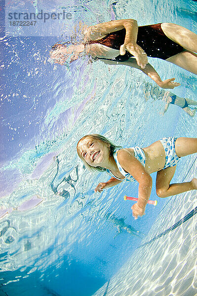 Ein junges Mädchen unter Wasser  während sie mit ihrer Mutter in einem Pool schwimmen lernt.