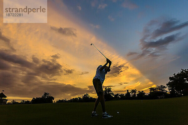Seitenansicht eines Mannes  der bei Sonnenuntergang Golf spielt