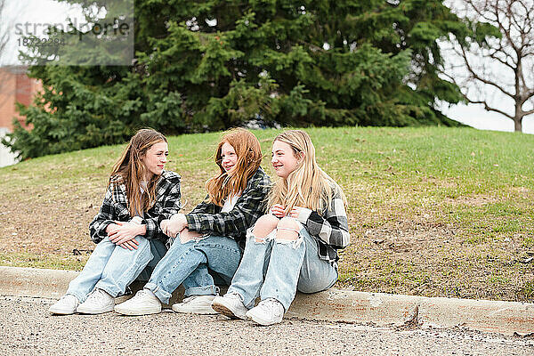 Drei glückliche Teenager-Mädchen sitzen auf einem Bordstein.