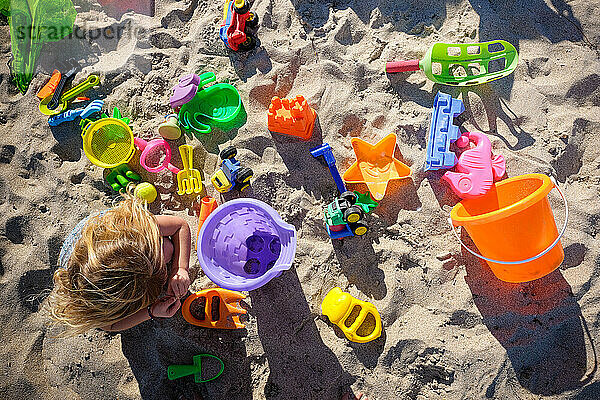 Blick von oben auf ein kleines Mädchen und all ihre ausgebreiteten Strandspielzeuge