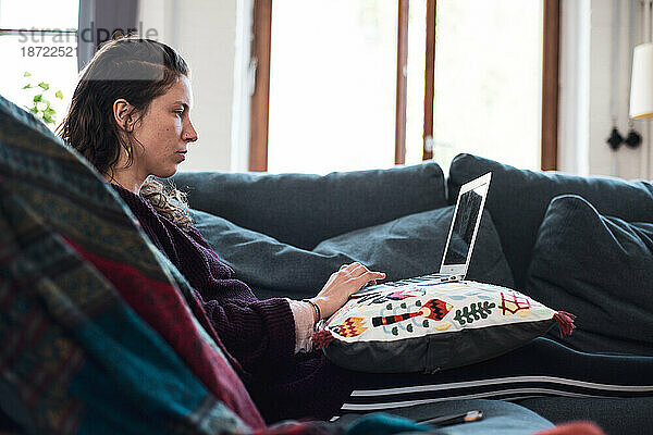 Frau am Laptop arbeitet von zu Hause aus in der bequemen Sofalounge