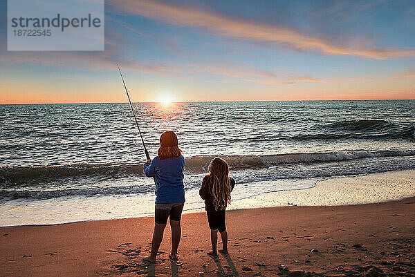 Zwei kleine Mädchen angeln im Meer bei Sonnenuntergang