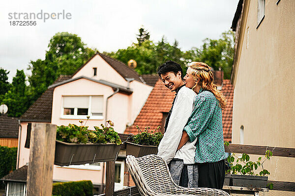 Gemischtes Rassenpaar lacht und umarmt sich auf dem Balkon im grünen deutschen Dorf