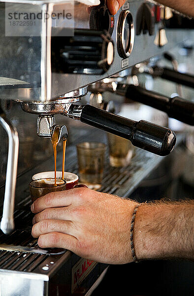 Detail einer Espressomaschine und eines Mannes  der eine Tasse hält.