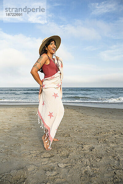 Latina-Frau amüsiert sich mit Handtuch und Hut am Strand