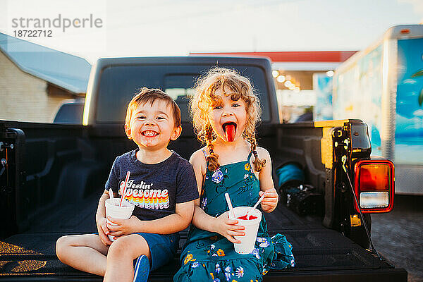 Fröhliche kleine Jungen und Mädchen  die im Sommer draußen sitzen und Schneekegel essen