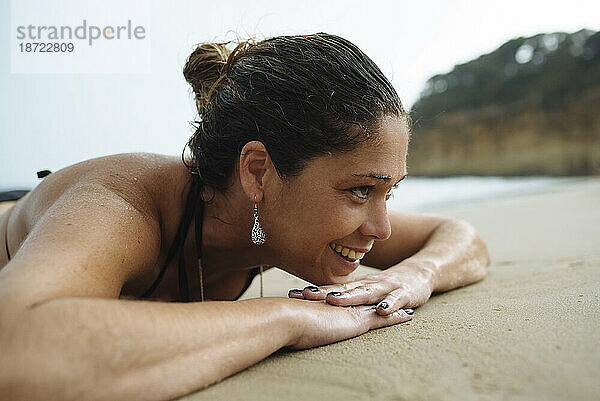 Nahaufnahmeporträt einer Frau  die auf dem Strandsand liegt.