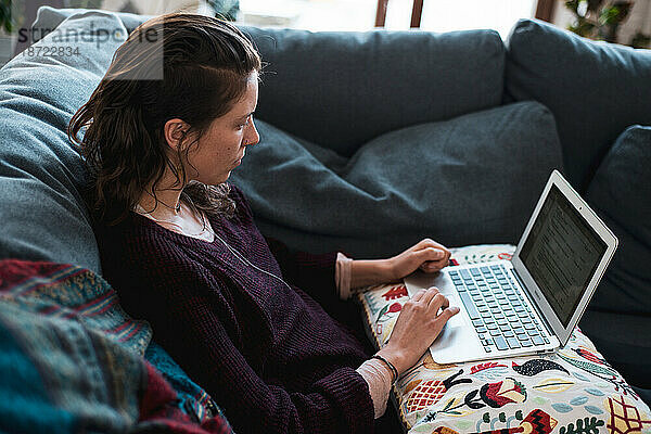 Entspannte Frau arbeitet von zu Hause aus am Computer auf dem Sofa