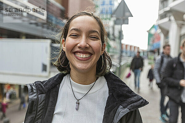 Lächelnde junge Frau gemischter Abstammung mit Piercing in Nase und Ohren auf der Straße.