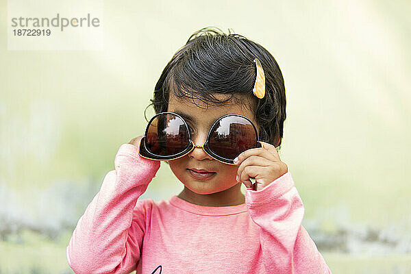 Nettes kleines Mädchen  das eine modische Sonnenbrille trägt und Spaß macht
