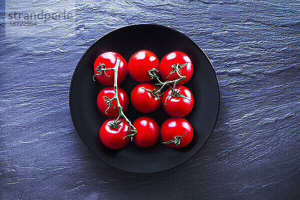 Draufsicht auf frische Tomaten auf schwarzem Teller vor Schiefer