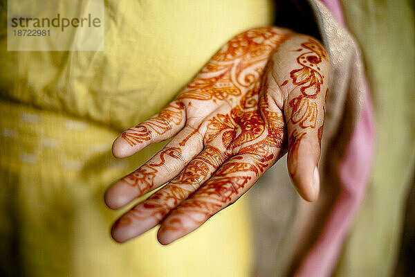 Detail des traditionellen indischen Henna auf der Handfläche eines Mädchens vor einem gelben Sari.