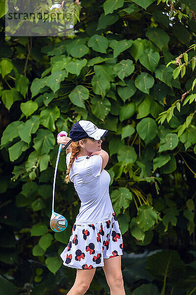 Seitenansicht einer jungen Frau mit Hut beim Golfspielen