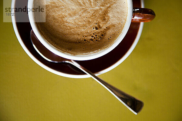 Ein Latte in einer Kaffeetasse auf einem bunten Tisch.