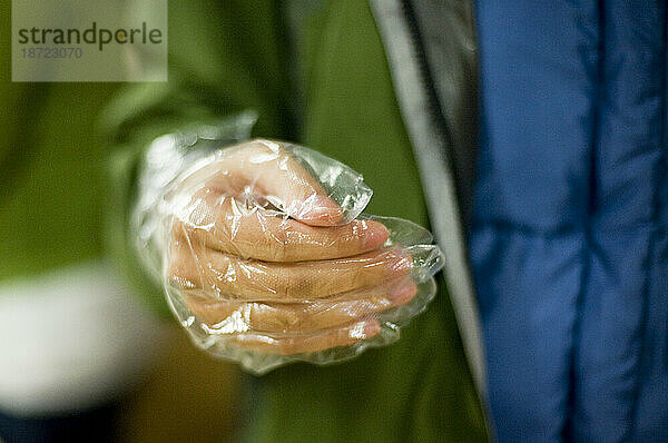 Detail einer Hand mit Plastikhandschuh in einer Suppenküche in San Francisco.