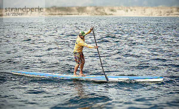 Ein junger Mann paddelt während eines Rennens auf einem Stand-Up-Paddleboard (SUP).