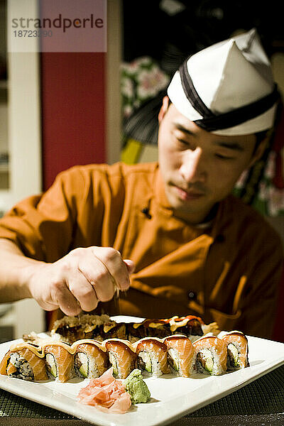 Ein Koch bereitet einen Teller Sushi zu.