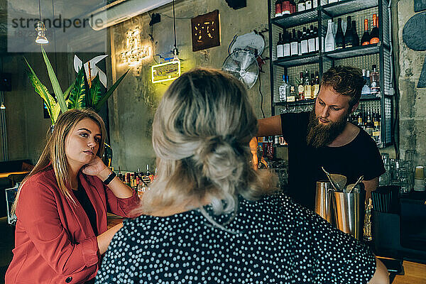 Zwei Freundinnen unterhalten sich und Barkeeper in einer Cocktailbar.