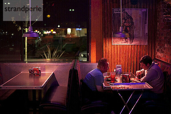 Zwei Männer sitzen an einem Tisch und essen Pizza in einem schwach beleuchteten Restaurant in Federal Way  Washington.