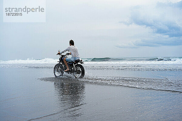 Mann fährt mit Motorrad am Meeresstrand.