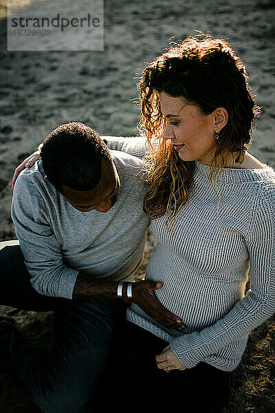 Mann und Frau umarmen sich  Mann berührt schwangeren Bauch am Strand