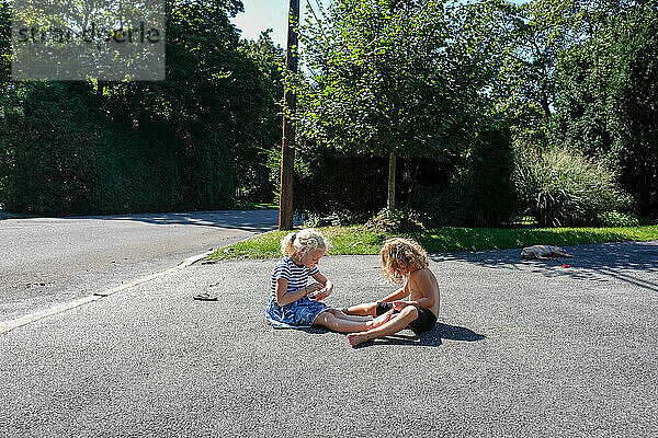 Zwei Kinder sitzen auf der Einfahrt und spielen im Sonnenlicht