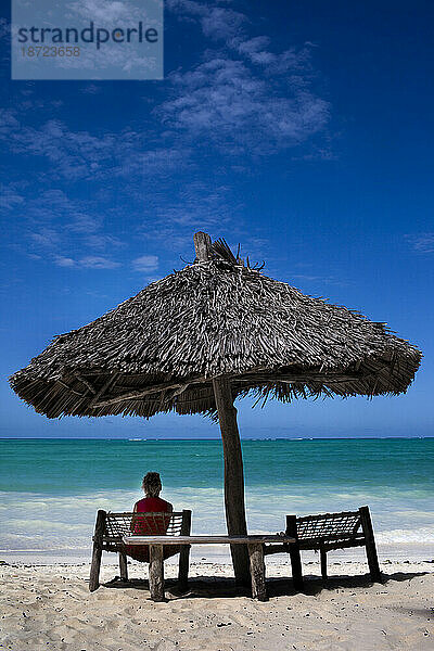 Ein Tourist sucht in Tansania Schutz vor der Sonne unter einem Sonnenschirm aus Palmenblättern.