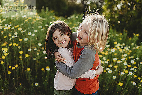 Junge und Mädchen im schulpflichtigen Alter umarmen sich im Blumenfeld