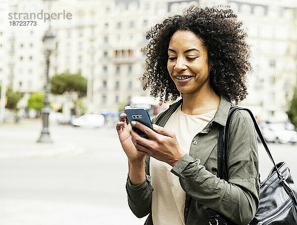 Nahaufnahme einer lächelnden Frau  die mit seinem Telefon auf der Straße SMS schreibt.