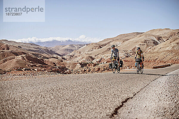 Zwei Bikepacker fahren eine Straße entlang  hinter sich Wüstenberge