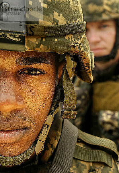 Soldaten stehen in einer gestapelten Formation mit dem Gesicht nach vorne. Sand und Schmutz bedecken ihre Tarnwesten und Helme.