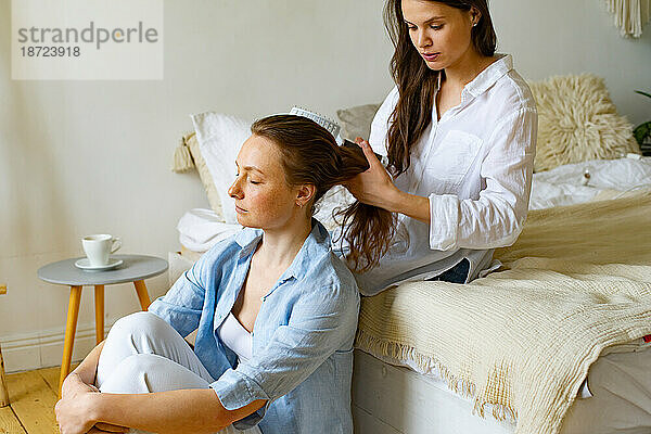 Zwei junge Frauen sitzen zu Hause zusammen  eine bürstet einer anderen die Haare