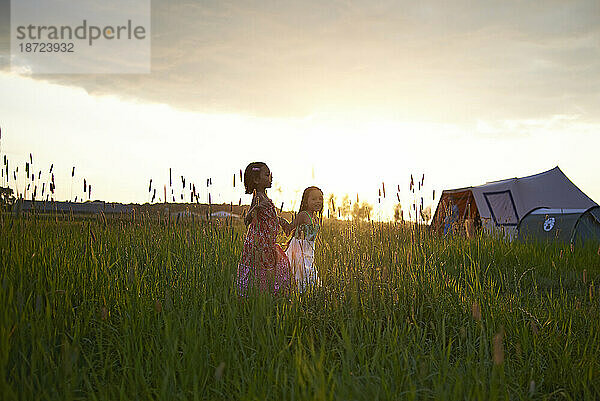 Zwei junge Mädchen laufen glücklich Hand in Hand durch ein Feld mit hohem Gras