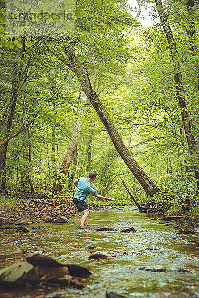Ein junger Mann wirft einen Stein flussabwärts  während er in einem Fluss steht.