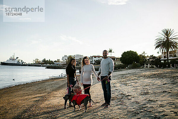 Patchwork-Familie mit Hunden  die bei Sonnenuntergang am Strand in die Kamera lächeln