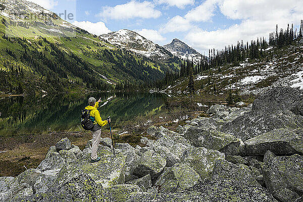 Rückansicht eines Wanderers mit Rucksack  der auf Berge und einen See zeigt
