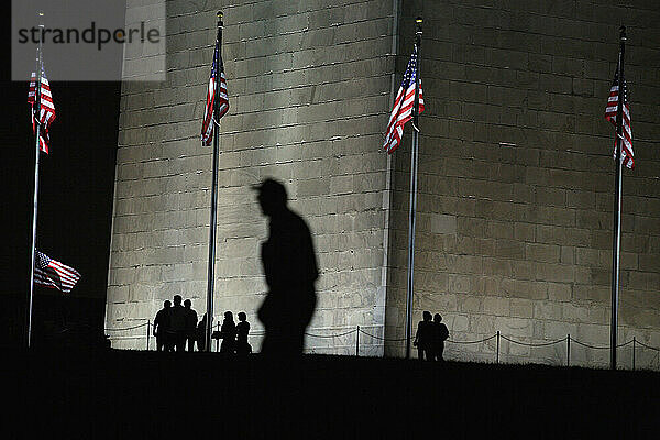 Silhouetten von Menschen  die an den leistungsstarken Lichtern vorbeigehen  die nachts auf dem Washington Monument in Washington  D.C. leuchten.