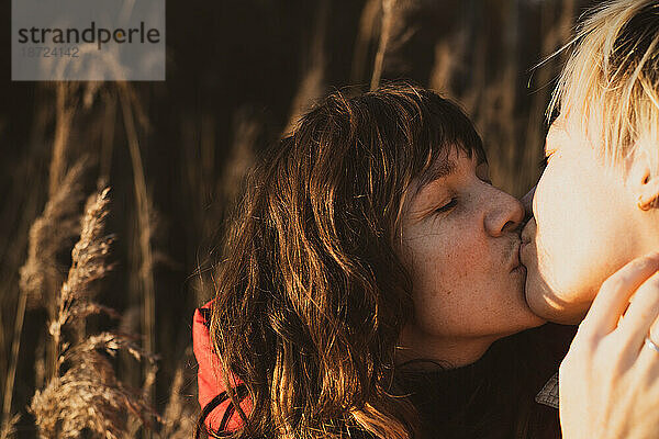 Queeres weibliches Paar küsst sich draußen in goldener Natur und Sonnenlicht