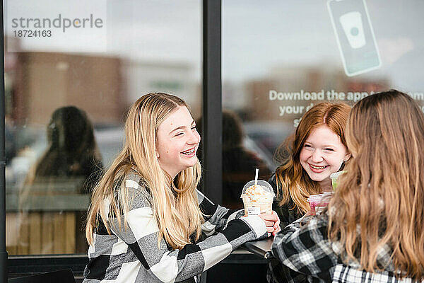 Drei glückliche Teenager-Mädchen trinken vor einem Café etwas.