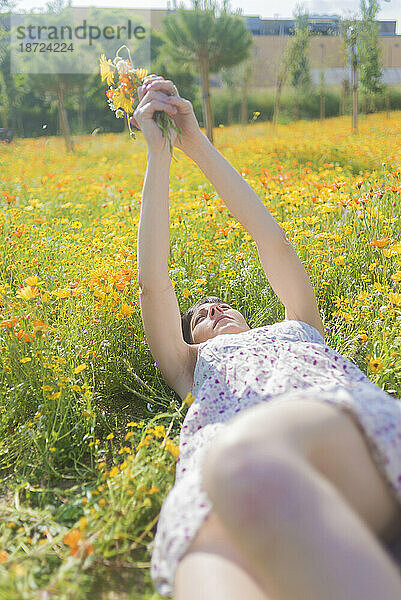 Draufsicht auf eine schöne Frau im Kleid  die auf einer Wiese liegt und an einem sonnigen Tag mit Blumen genießt