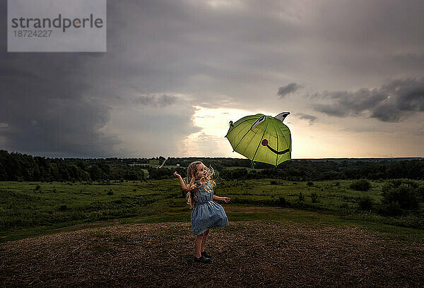 Kleines Mädchen mit Regenschirm unter stürmischem Himmel