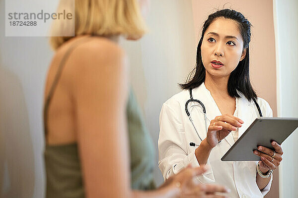 Ärztin hält Tablet-PC in der Hand  während sie mit dem Patienten spricht
